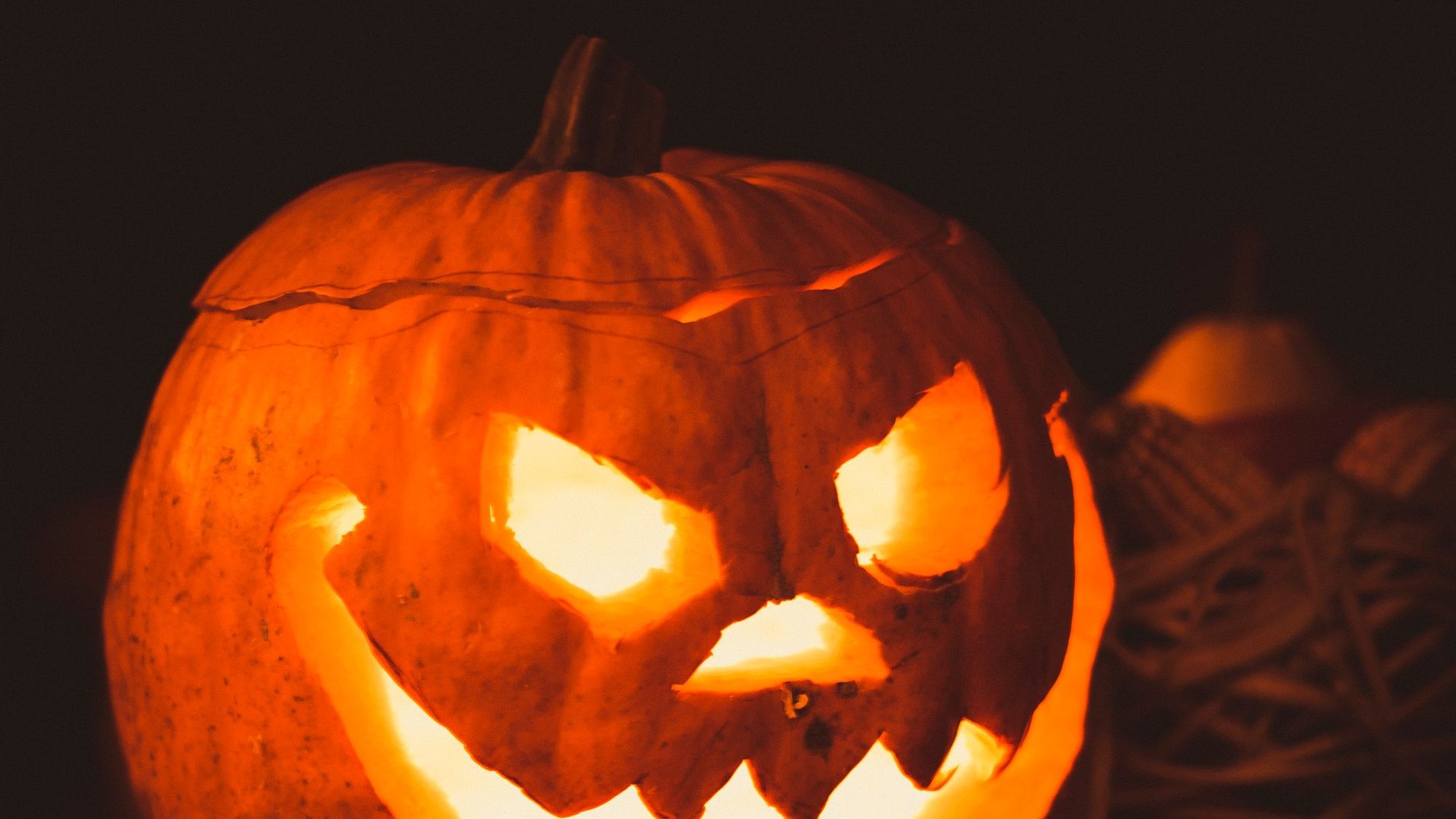 A carved pumpkin glowing orange from inside against a dark background (illustrative stock photo).