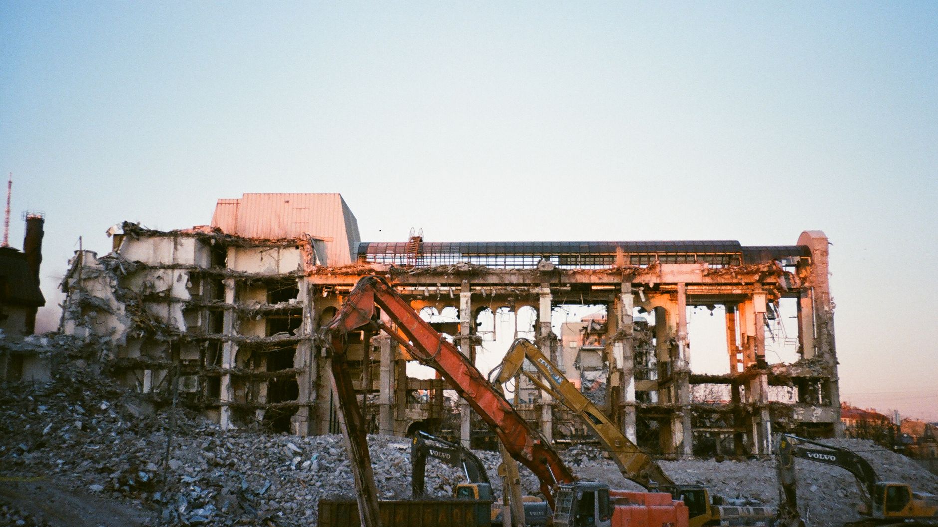 Yellow and orange excavators among the rubble of a partly demolished multi-storey building at sunset (illustrative stock photo).