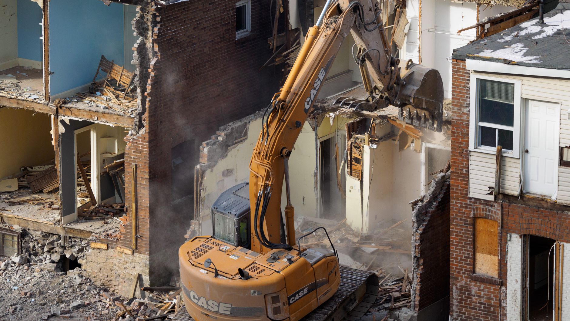An excavator pulling apart the front of a brick terrace house, with debris below (illustrative stock photo).