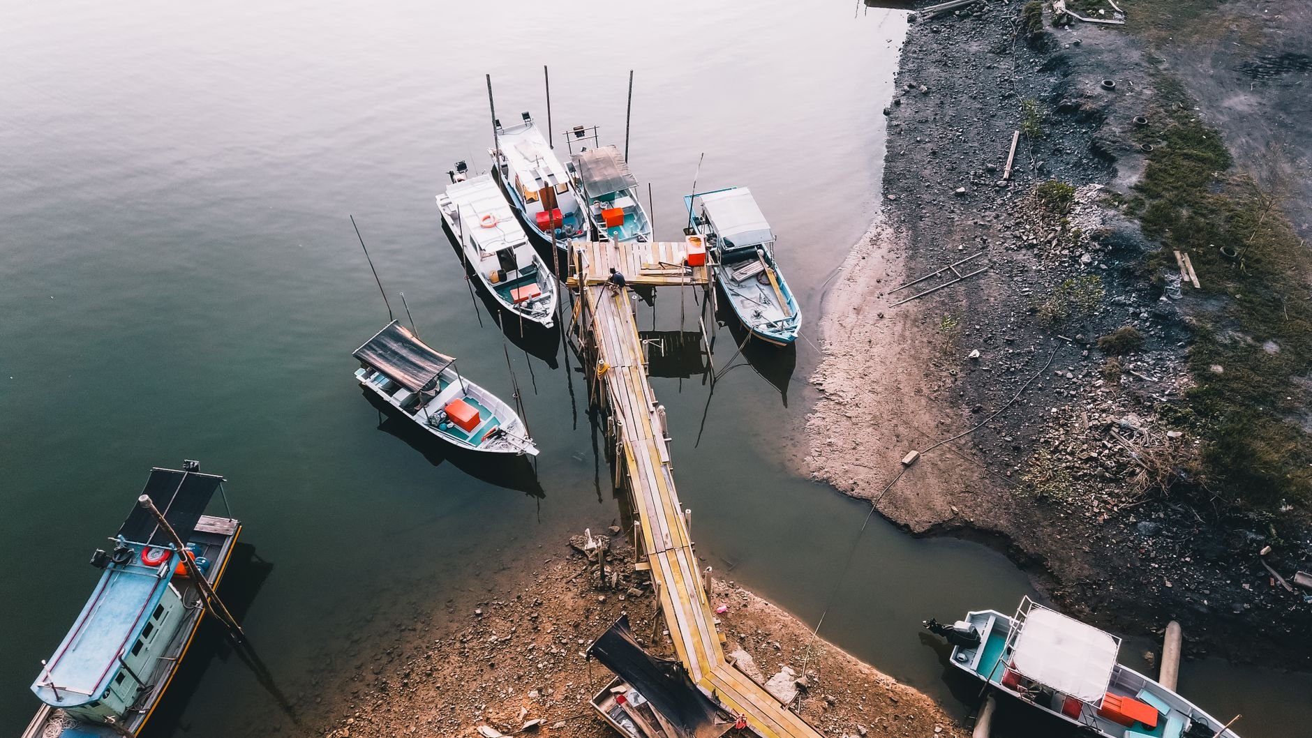 Small fishing boats moored beside a wooden pier on calm, dark water (illustrative stock photo).