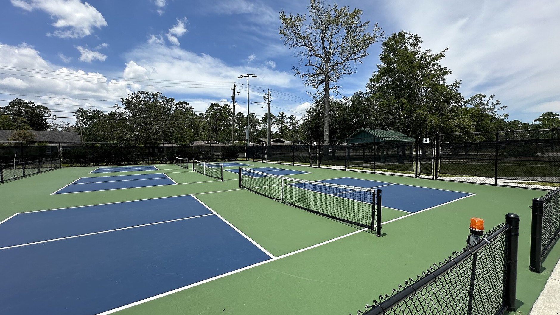 Blue and green outdoor pickleball courts behind black fencing under a cloudy sky (illustrative stock photo, not in Hua Hin).