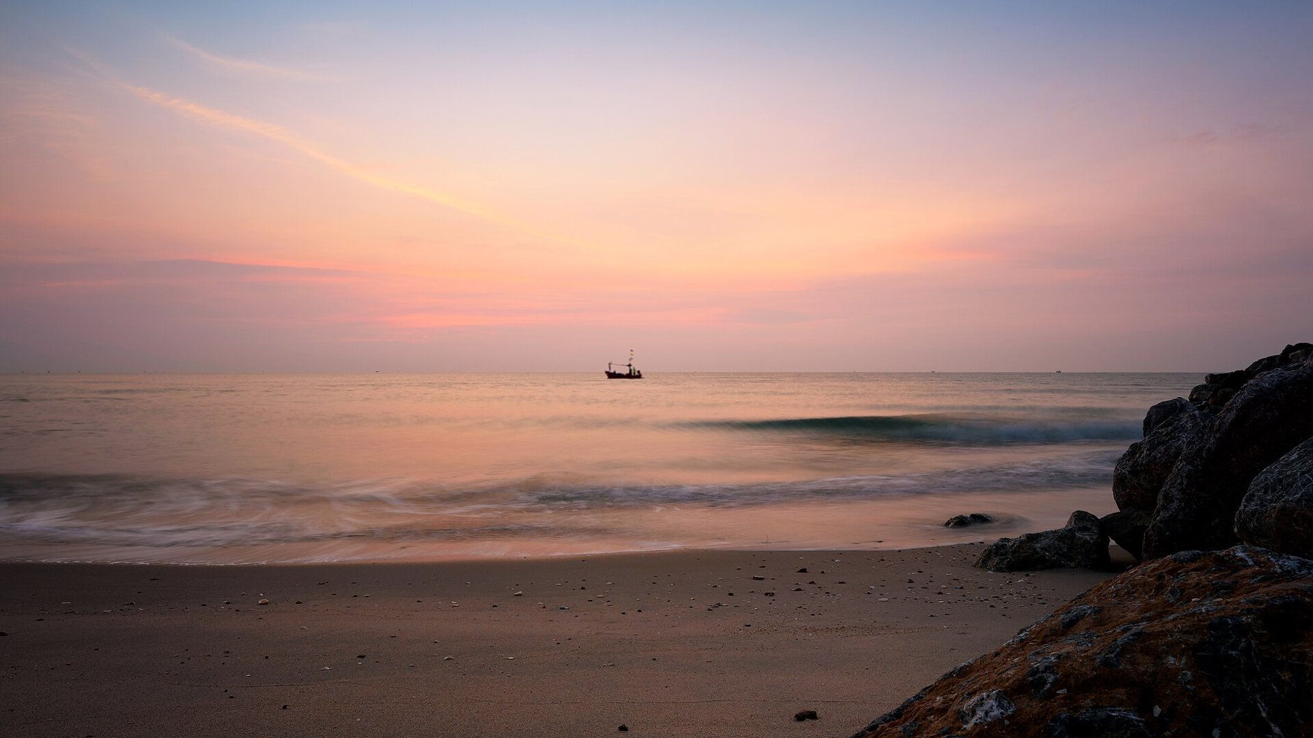 A fishing boat on the horizon at sunrise, with soft pink light over the Gulf of Thailand near Hua Hin.